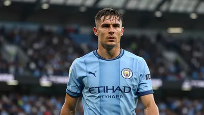 Mid-30s muscular defender, waist-up, intense gaze, sky-blue and navy Manchester City home shirt, crest crisp on left...