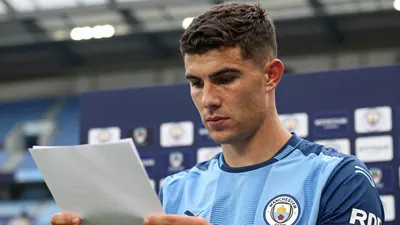 A close-up of a tall, 28-year-old, dark-haired Manchester City midfielder with a strong jawline, wearing the sky blue and...
