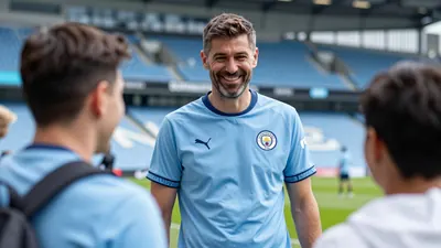 A beaming, mid-30s Manchester City coach, in a sky blue and navy home kit with the Citizens' crest on his chest, smiles...