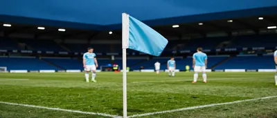A rainy evening street outside a stadium, a crowd of anonymous Manchester City supporters in plain sky-blue hoodies and...