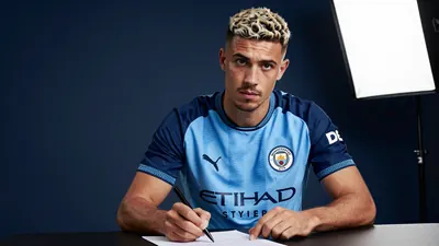 A 30-year-old Manchester City midfielder, with a strong build and determined expression, signs a contract, wearing the...